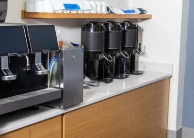 Beverage station with beverage dispensers, insulated beverage carafes, custom wood shelves with cups, and custom wood under-counter cabinets.