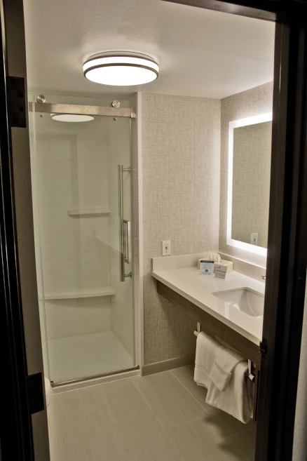 Renovated hotel bathroom with new tile flooring and walls, shower, vanity, lighting, and fixtures. 