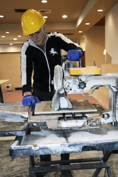 Tile contractor wearing safety gear cutting tiles to install in the Holiday Inn Yakima lobby bathroom.