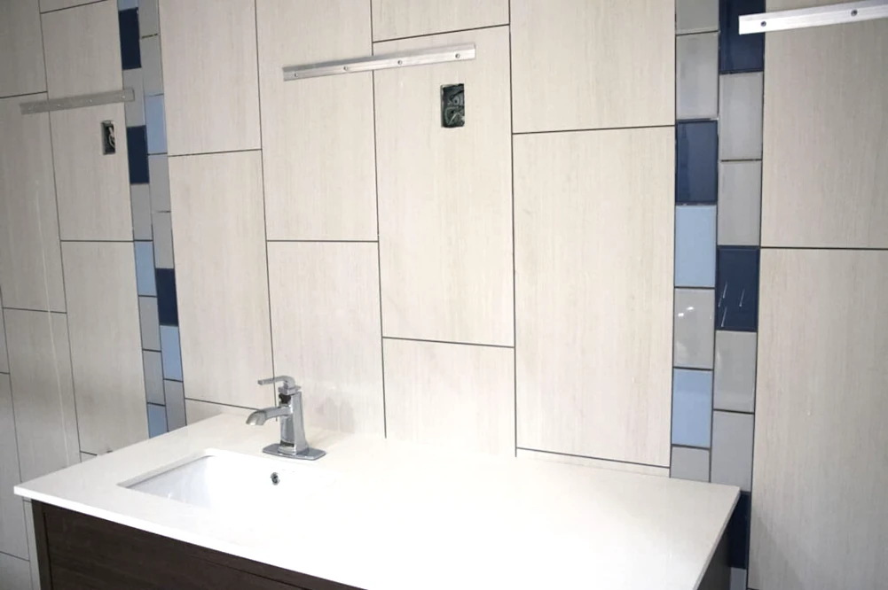 Renovated Holiday Inn Yakima lobby bathroom with new sink, quartz-topped vanity, white, navy, blue, and grey tile walls, and fixtures to hang mirrors. 